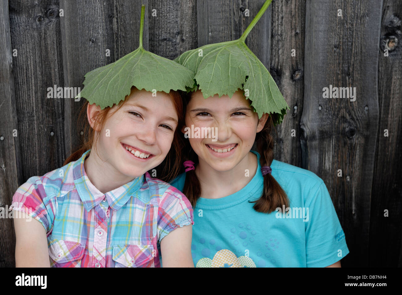 Deux jeunes filles, 11 ans, avec des feuilles sur la tête, feuilles de tussilage (Tussilago tussilage), parasols naturels Banque D'Images
