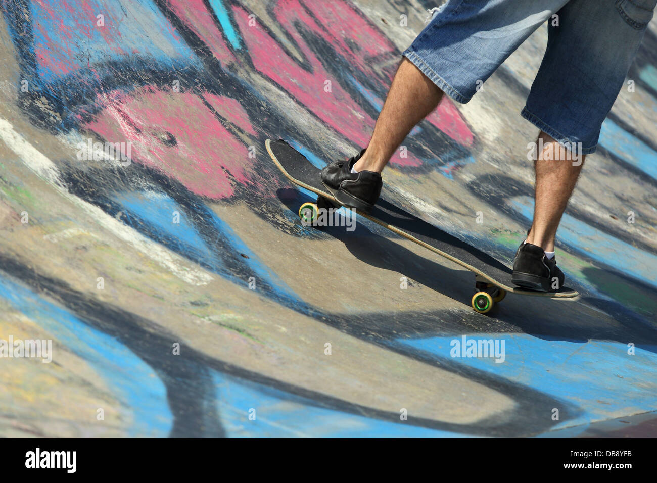 Garçon jambes sur une planche à roulettes dans un half pipe avec graffiti Banque D'Images