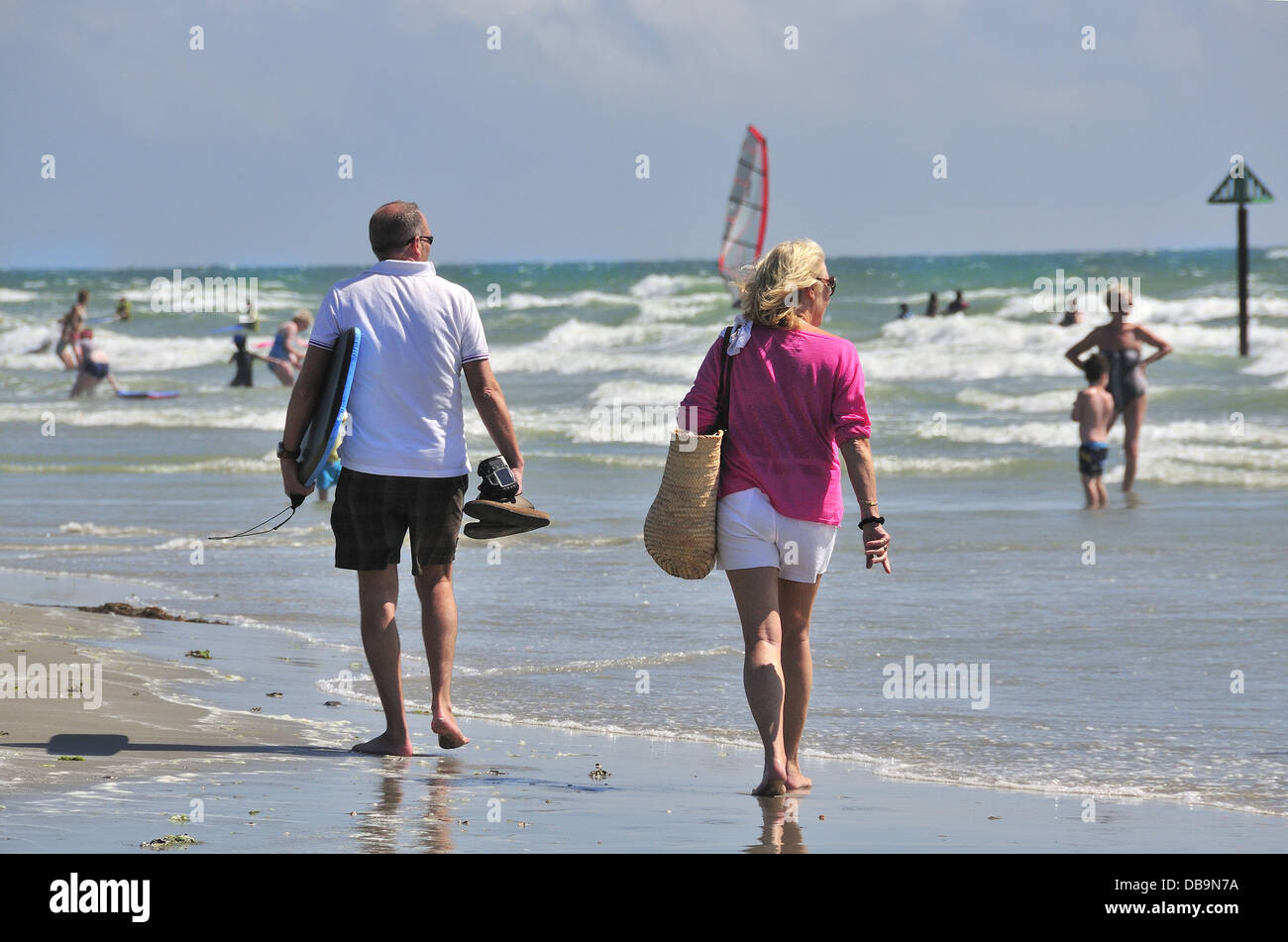 Couple on chaude journée à West Wittering plage pavillon bleu, nr. Chichester, West Sussex, UK regarder les vacanciers profiter de la baignade. Banque D'Images