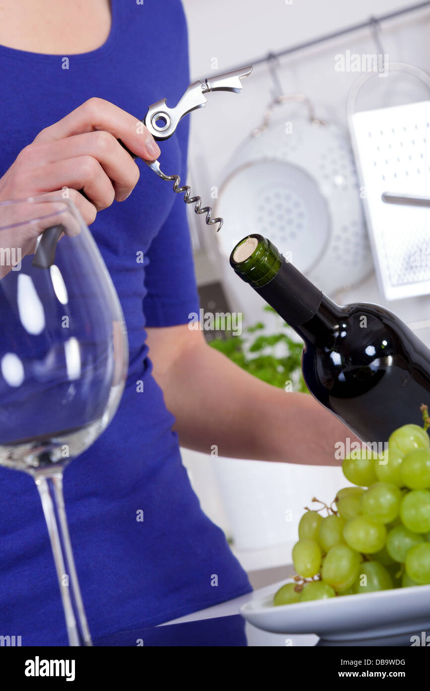 Jeune femme l'ouverture d'une bouteille de vin rouge dans sa cuisine moderne Banque D'Images