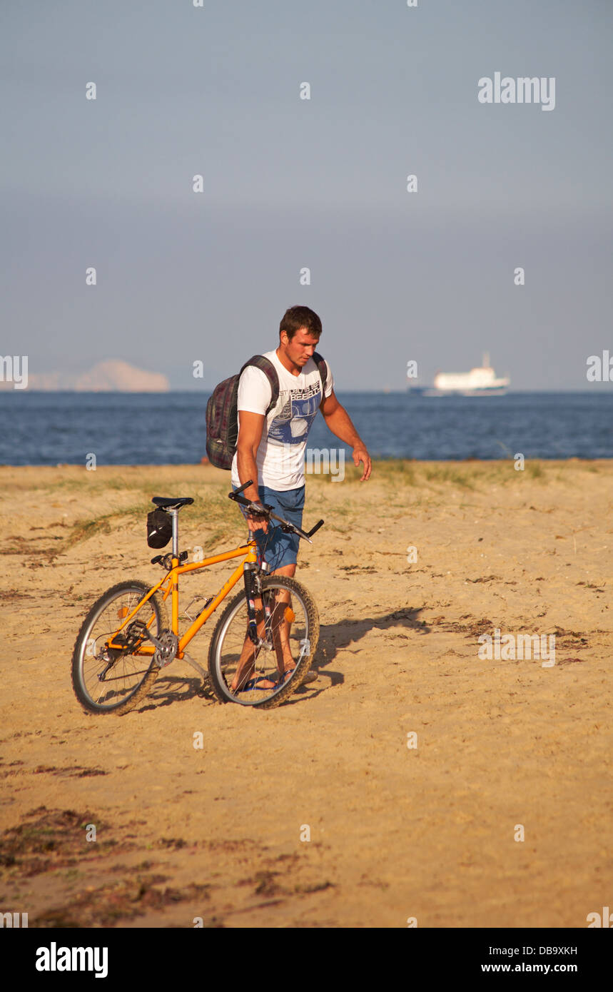 Beau jeune homme poussant vélo le long de la plage Studland du flou voile et les falaises en arrière-plan sur soirée Juillet ensoleillé Banque D'Images