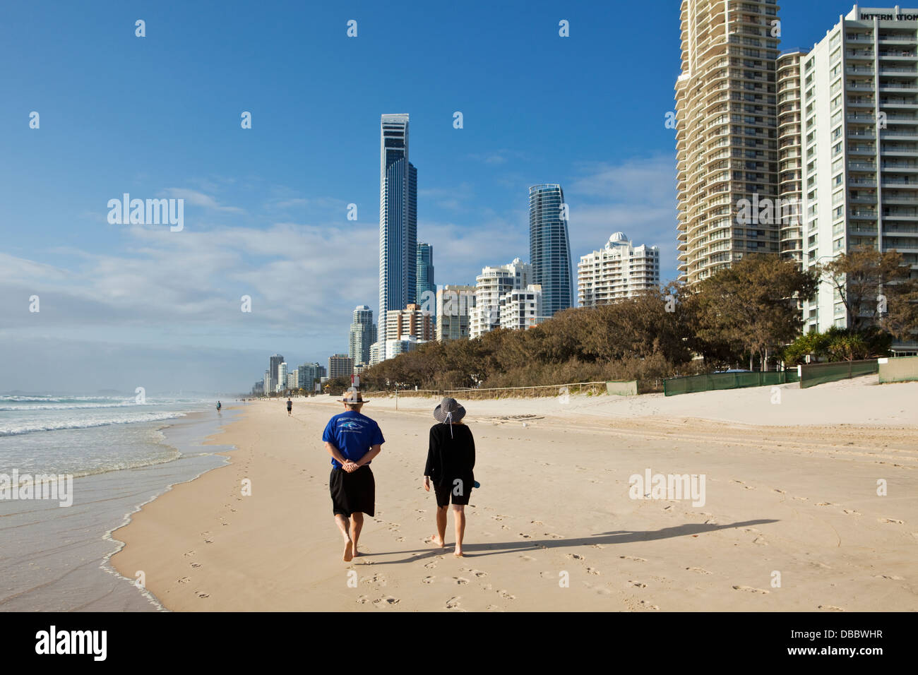 Couple en train de marcher le long de plage avec des toits de la ville en arrière-plan. Surfers Paradise, Gold Coast, Queensland, Australie Banque D'Images
