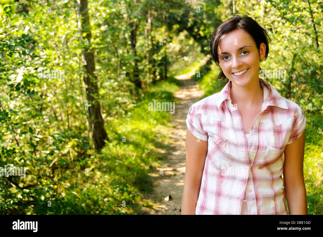 A smiling young woman wearing vêtements de montagne sur un sentier pédestre dans le bois Banque D'Images