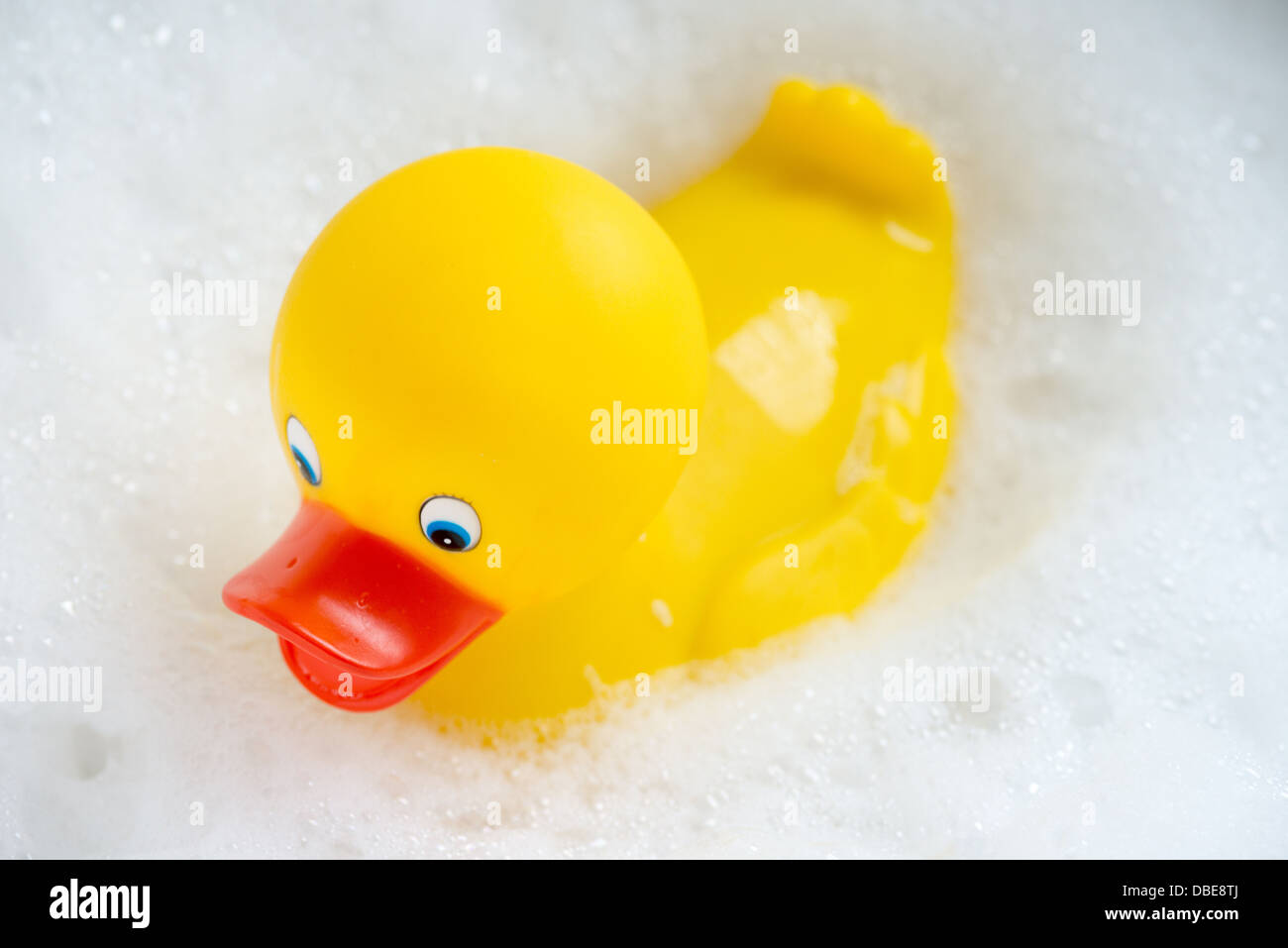 Un canard en caoutchouc jaune vif flottant dans les bulles blanches d'un bain à bulles. Banque D'Images