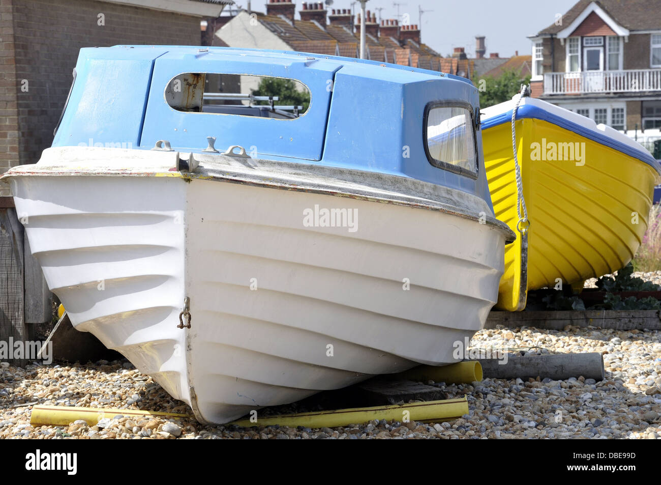 Bateau bleu et blanc sur la plage de galets avec bateau jaune derrière Banque D'Images