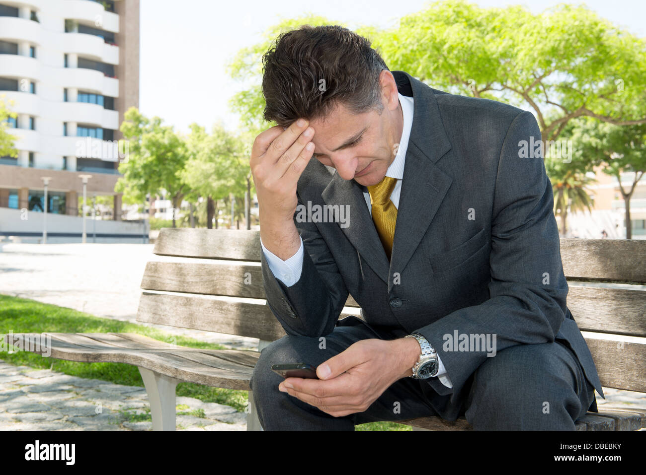 Inquiets businessman in a park bench with cellphone Banque D'Images