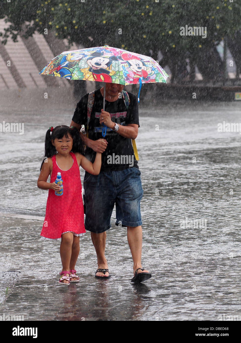 Père et fille s'abritant sous leur égide pendant une averse de pluie à Hong Kong Banque D'Images