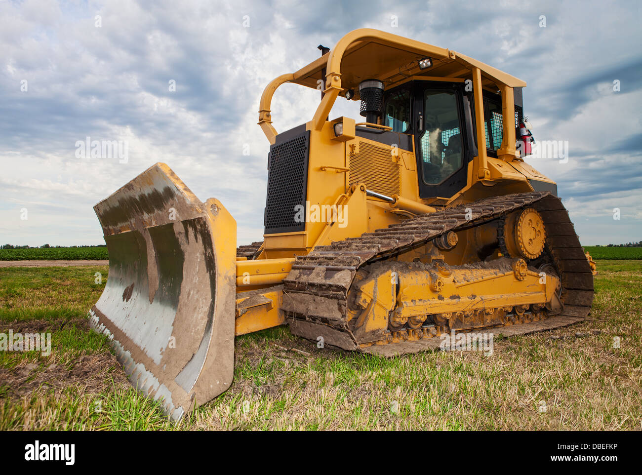 Un grand bulldozer jaune sur un chantier de construction à proximité d'un champ d'agriculteurs Banque D'Images