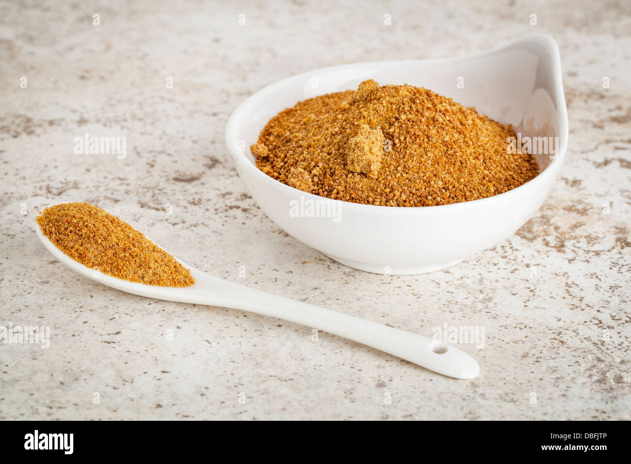 Petit bol en céramique de sucre non raffiné de cocotier contre un arrière-plan en céramique avec une cuillère Banque D'Images