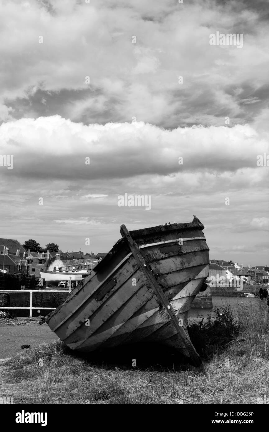 Image en noir et blanc d'un vieux bateau, couché sur l'herbe près d'un port avec ciel nuageux Banque D'Images