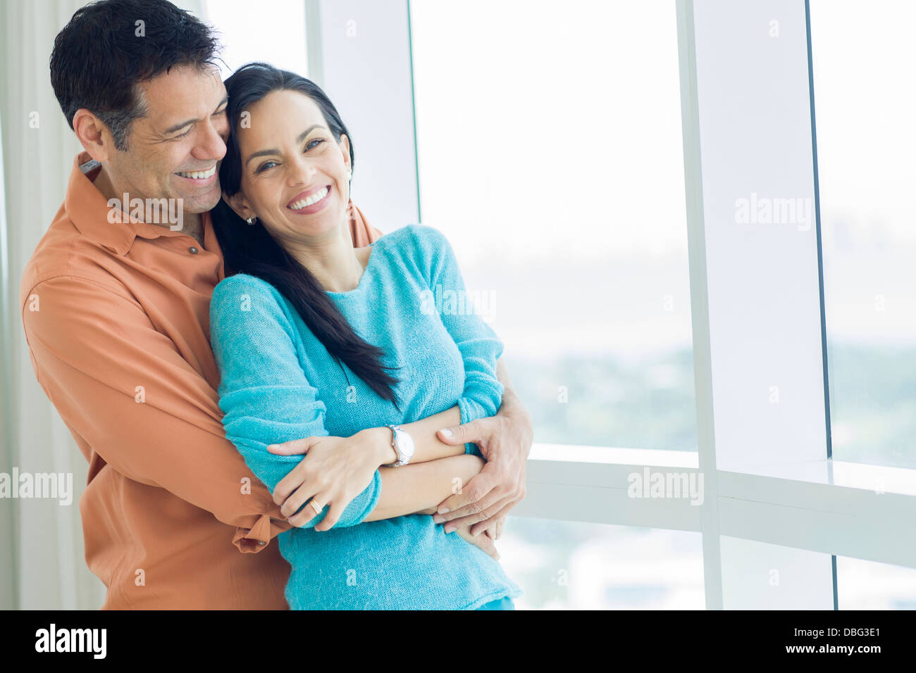 Hispanic couple hugging at window Banque D'Images