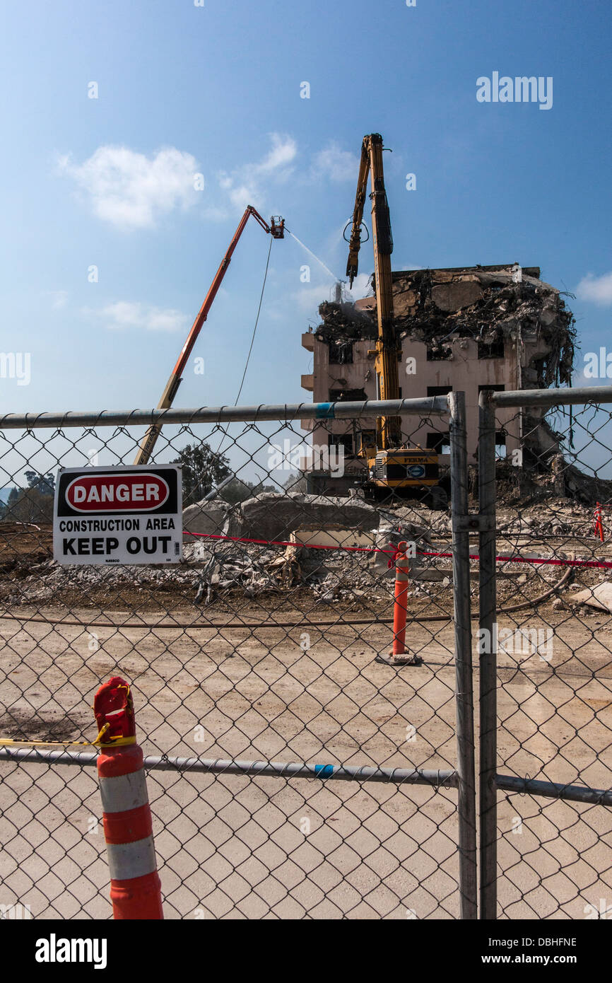 Le signe de danger sur la clôture avec la démolition de bâtiments en arrière-plan par excavatrices à l'ancien hôpital Eden à Castro Valley, en Californie. Banque D'Images