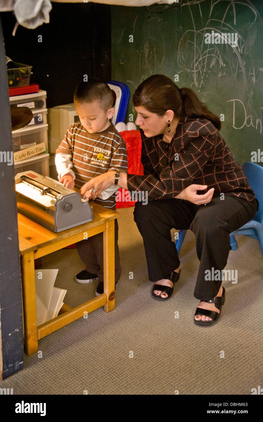 Avec l'aide d'un membre du personnel formé un garçon aveugle sur une machine à écrire braille types au centre d'apprentissage des enfants aveugles Banque D'Images