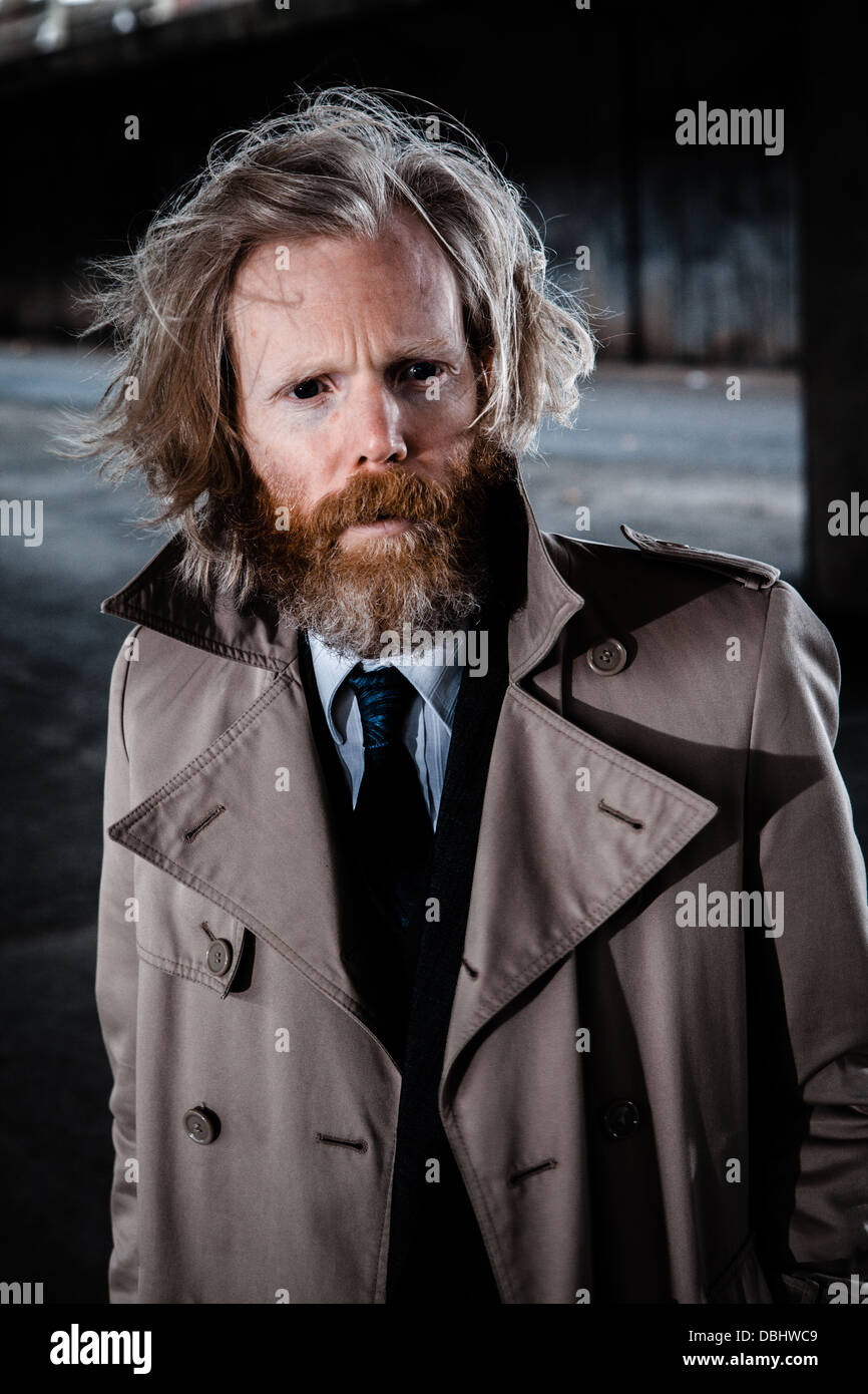 Homme barbu en costume et manteau dans un béton, urbain. Banque D'Images