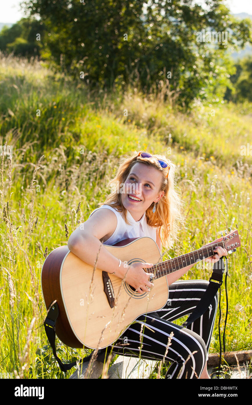Adolescente qui joue de la guitare dans les champs. À l'extérieur. L'été. Banque D'Images