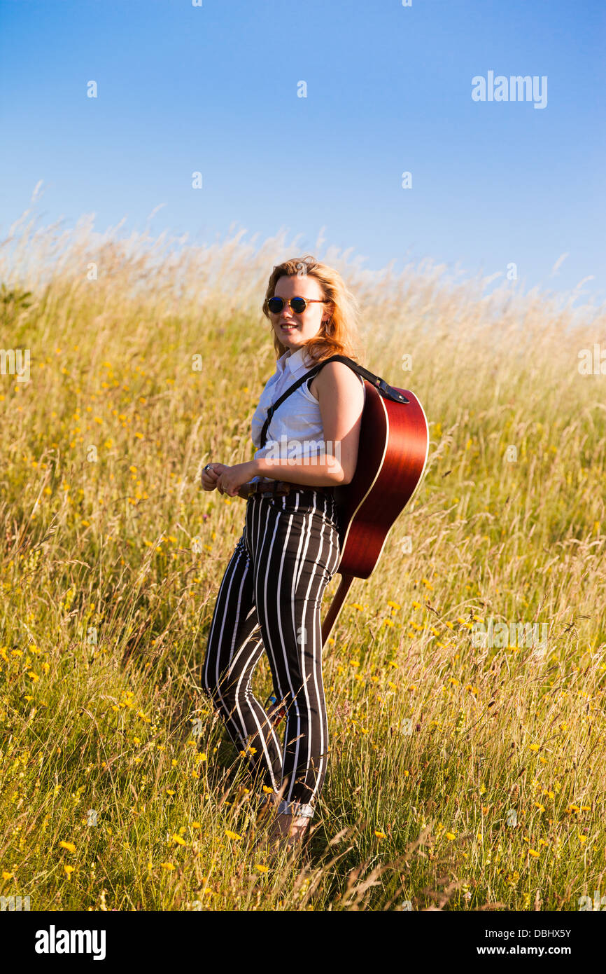 Adolescente marchant à travers les champs portant une guitare. À l'extérieur. L'été. Banque D'Images