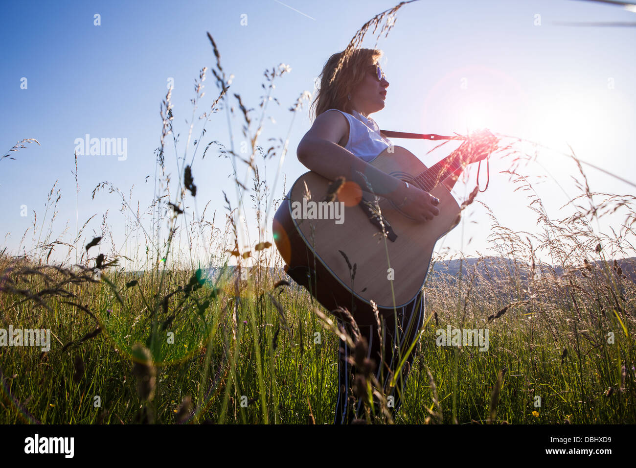 Teenage girl wearing lunettes noires jouant de la guitare dans les champs. À l'extérieur. L'été. Banque D'Images