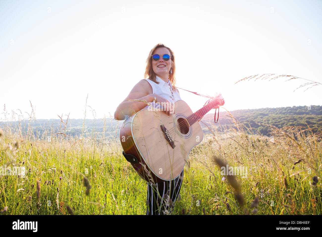Teenage girl wearing lunettes noires jouant de la guitare dans les champs. À l'extérieur. L'été. Banque D'Images