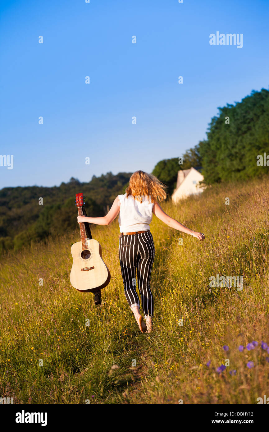 Adolescente marchant à travers les champs portant une guitare. À l'extérieur. L'été. Banque D'Images
