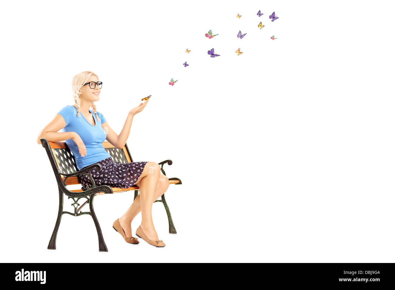 Jeune femme assise sur un banc en bois et à la recherche de papillons colorés isolé sur fond blanc Banque D'Images