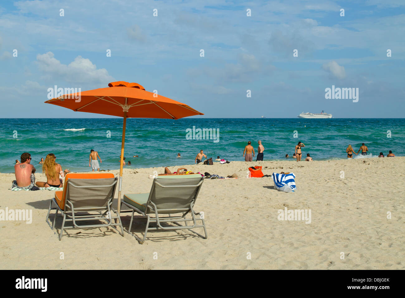 Chaises de plage, parasol orange et beaucoup d'heureux amateurs de plage à South Beach, Miami, Floride. Un bateau de croisière est dans la distance. Banque D'Images