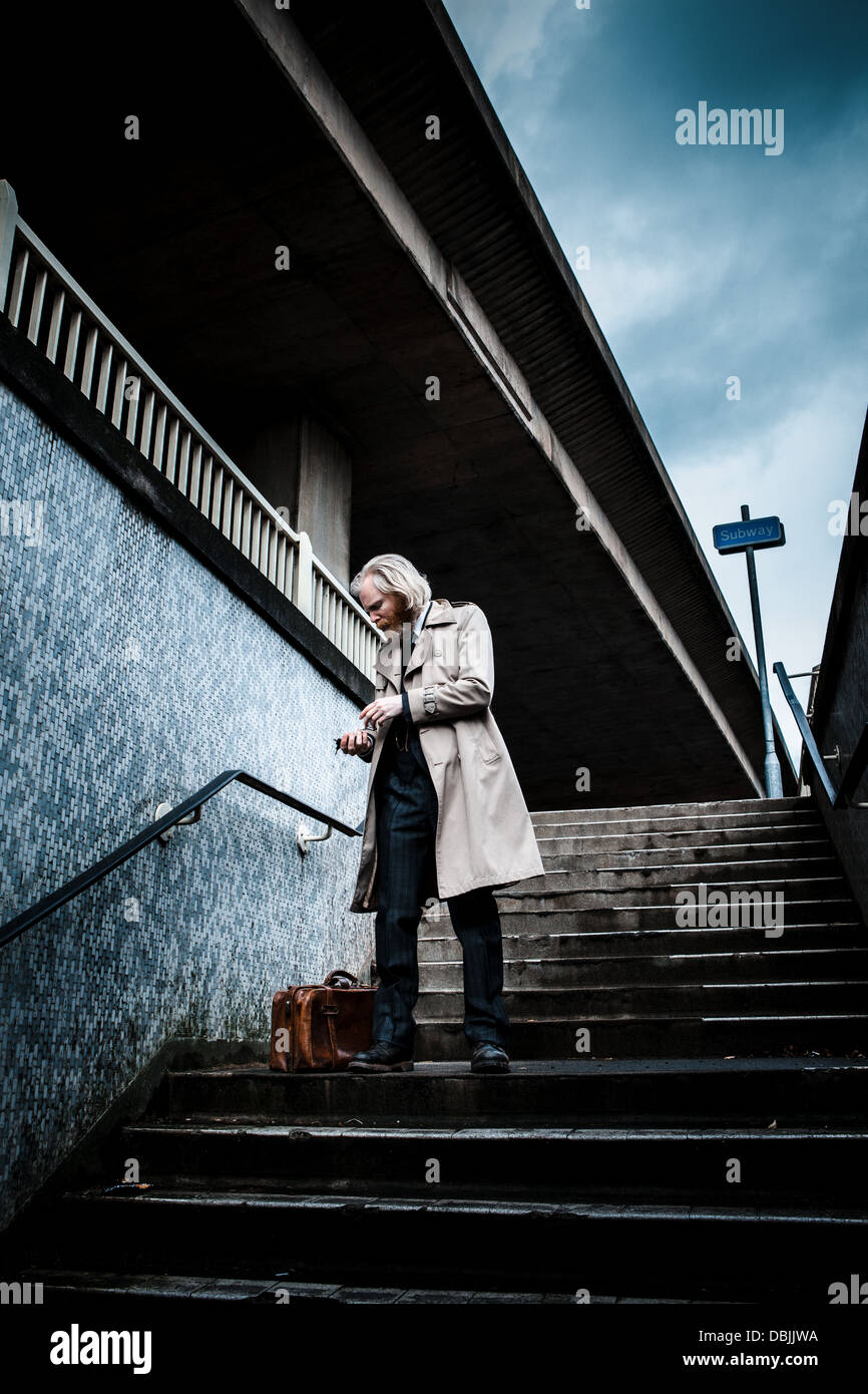 Homme barbu en costume et manteau tenant un vieux cartable en cuir walking down steps dans un métro. Banque D'Images