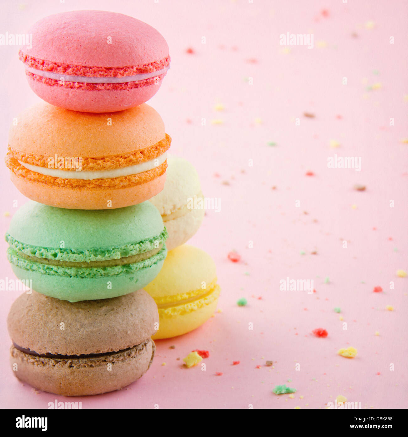 Pile de macarons colorés sur fond rose pastel avec de petites miettes Banque D'Images