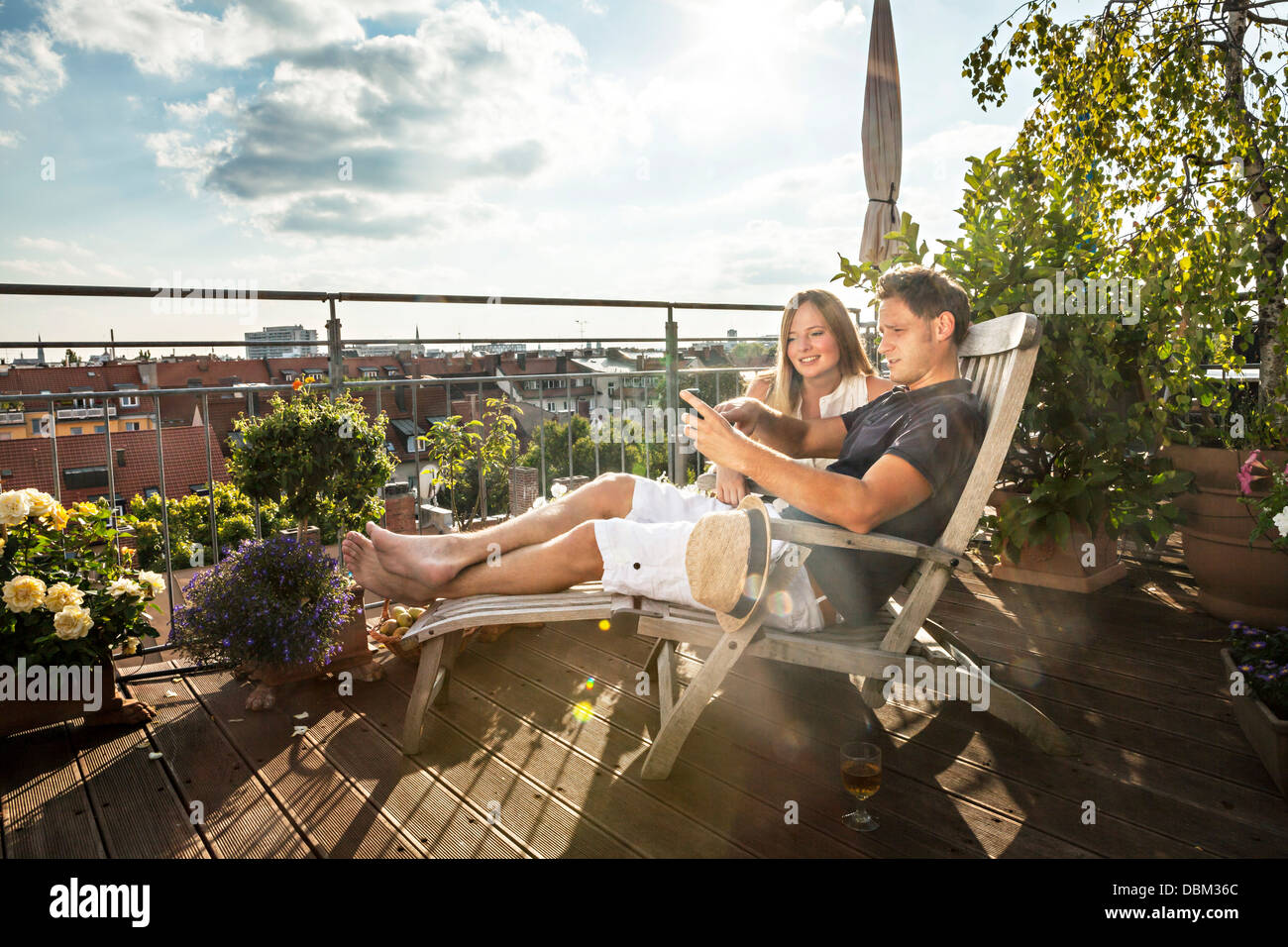 Couple sur balcon à l'aide de téléphone mobile, Munich, Bavaria, Germany, Europe Banque D'Images