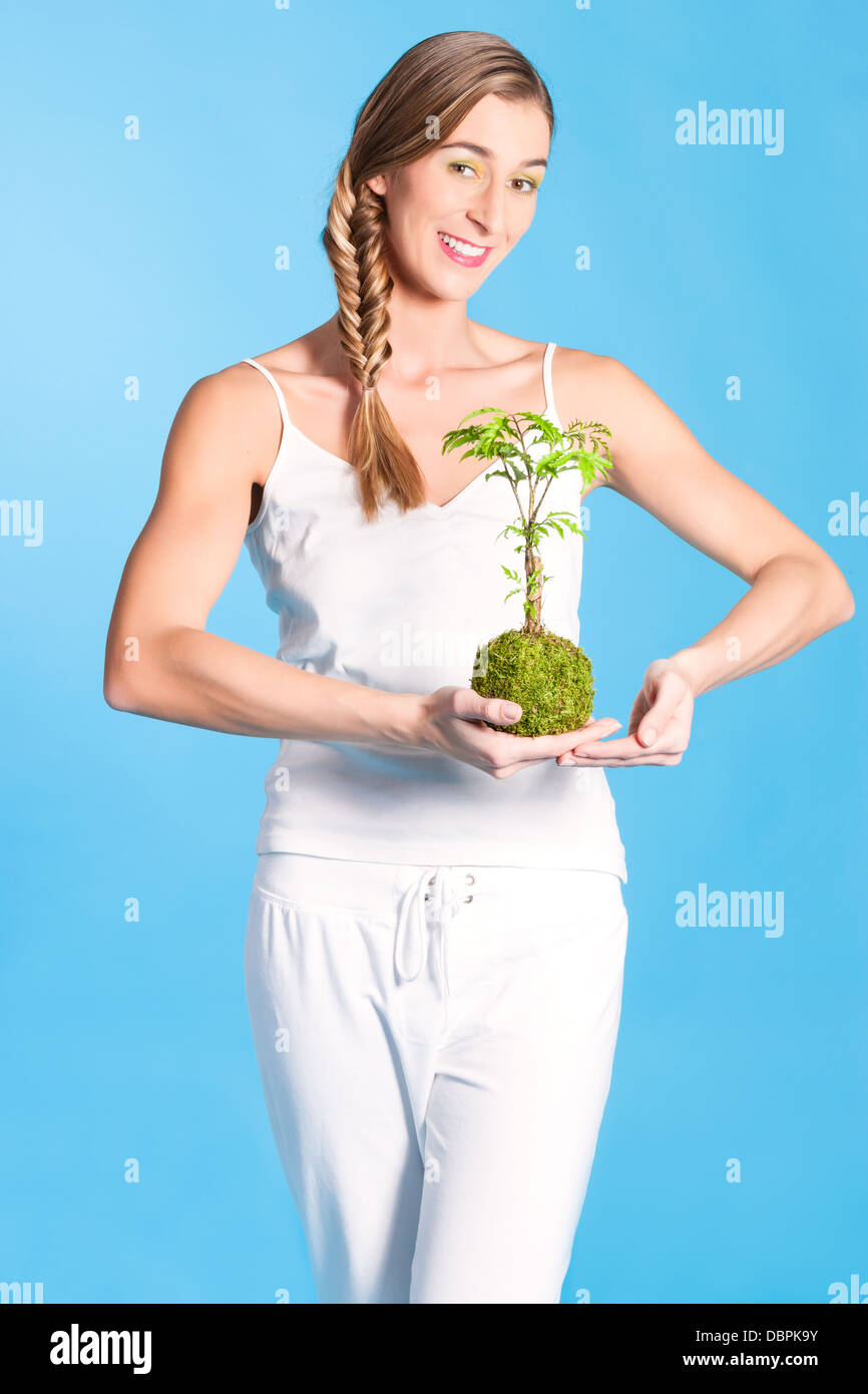 Jeune femme tenant un petit arbre symbolique, un symbole pour la protection et le soin de notre environnement, de la forêt et du monde Banque D'Images