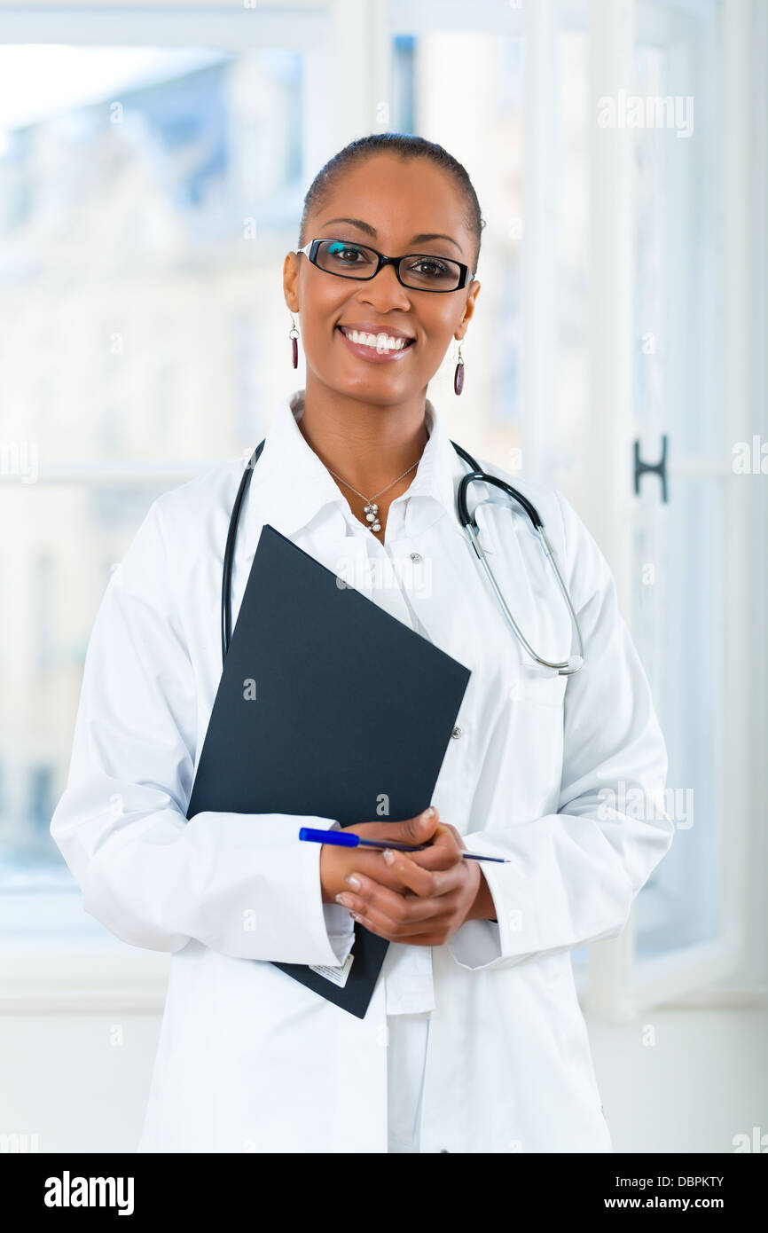 Jeune femme médecin noir debout à une fenêtre en clinique avec un fichier ou dossier Banque D'Images Jeune femme médecin noir debout à une fenêtre en clinique avec un fichier ou dossier Banque D'Images