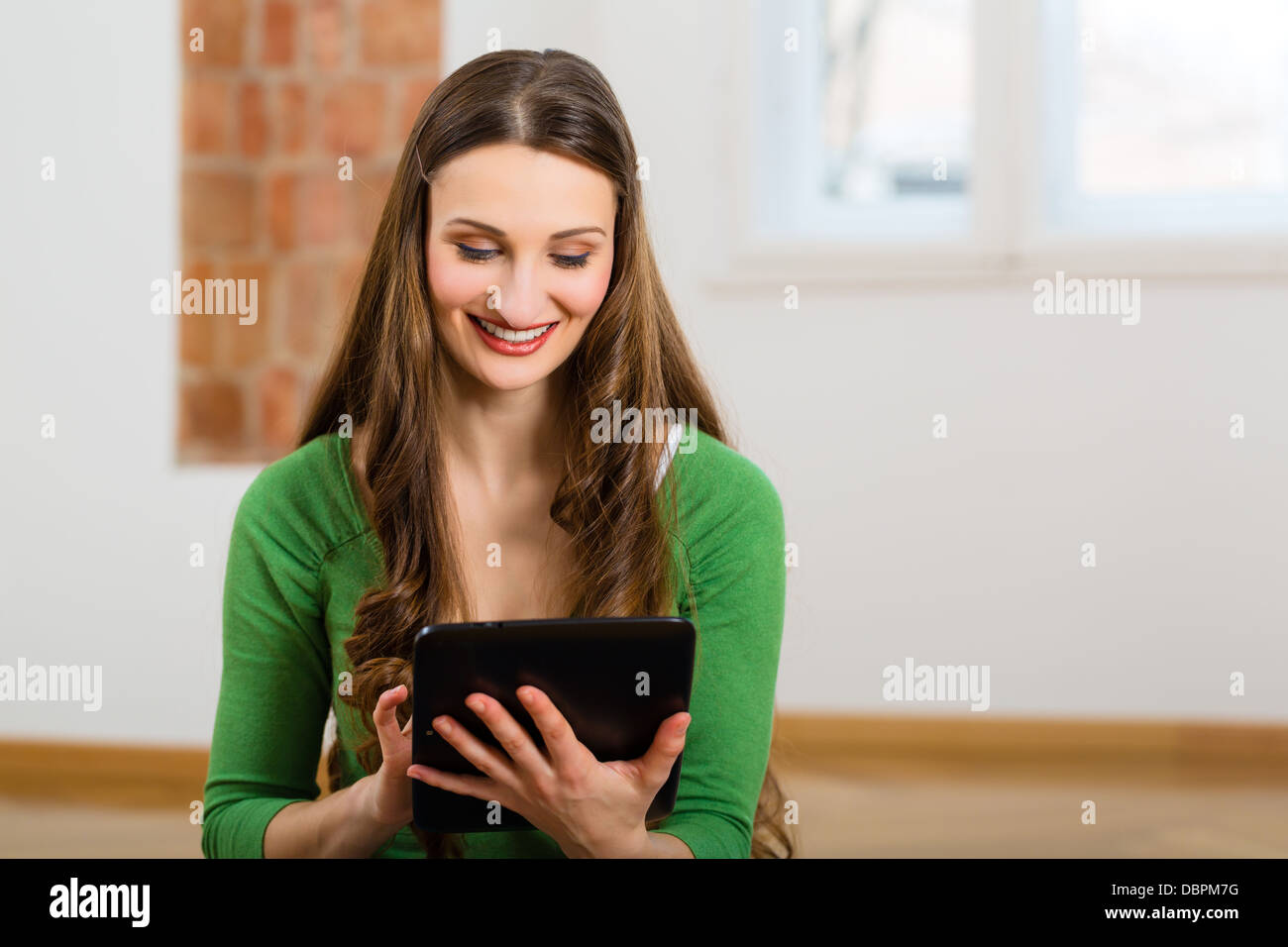 En ligne datant - Jeune femme assise à la maison sur le plancher et l'achat de nouveaux meubles sur Internet en utilisant un ordinateur tablette Banque D'Images