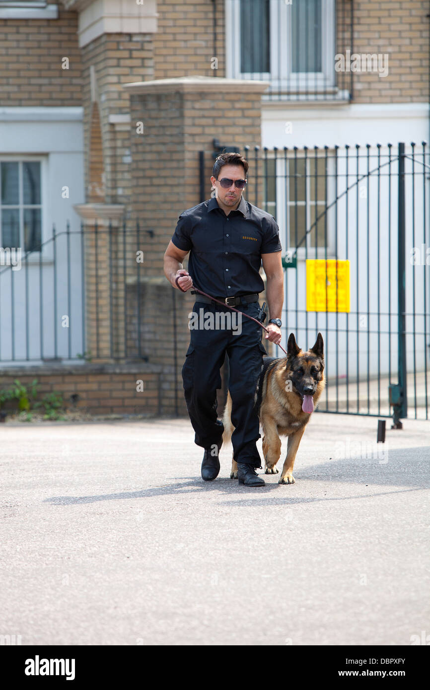 Burly garde de sécurité en patrouille avec chien de garde berger allemand devant les barrières de sécurité Banque D'Images