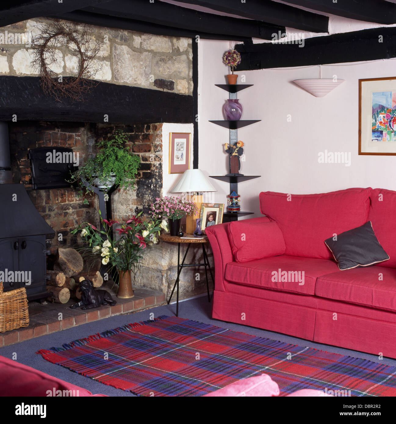 Canapé rose et bleu +rouge tapis tartan en face de cheminée avec poêle à  bois dans salon cottage Photo Stock - Alamy