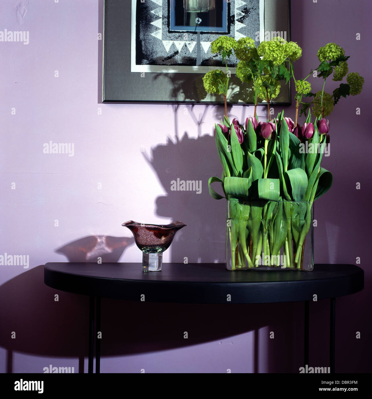 Tulipes mauve et vert-lime hortensias en vase en verre noir sur table console avec vase en verre violet dans la salle à manger moderne Banque D'Images