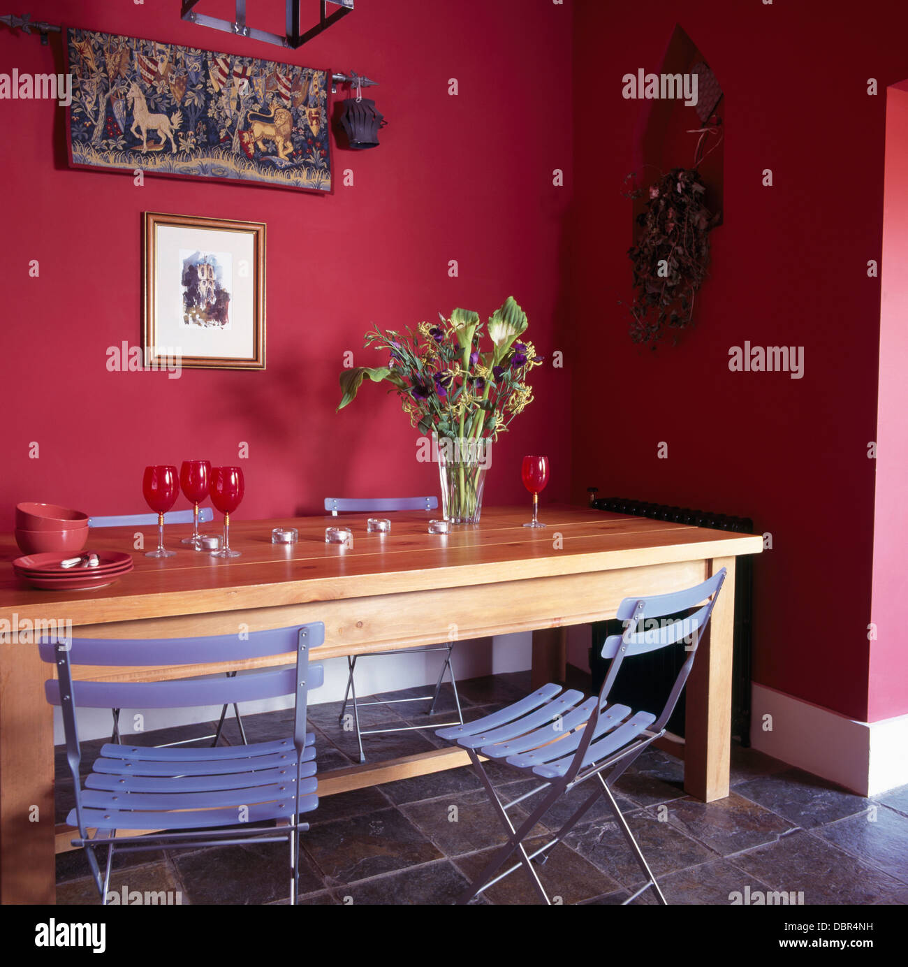Des chaises en plastique pliable bleu IKEA à table en bois simple rose vif en salle à manger avec sol en ardoise Banque D'Images