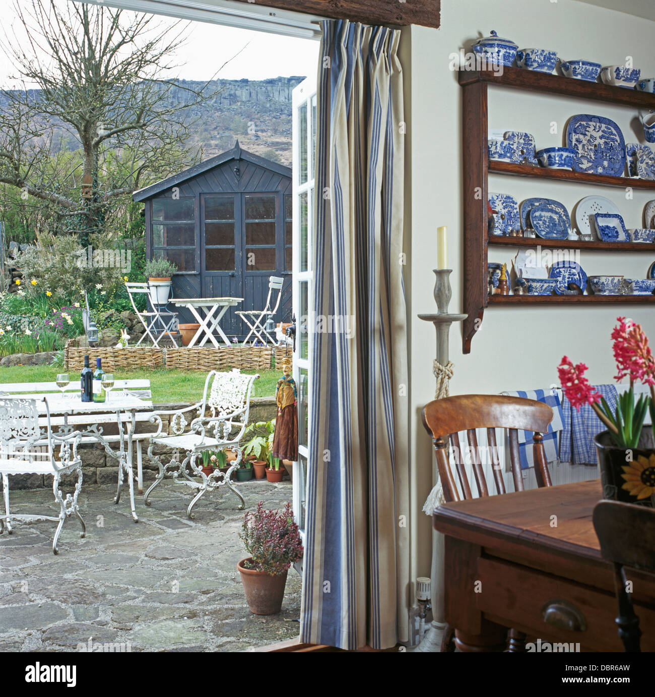 Vue sur patio grâce à ouvrir les portes en verre de cottage salle à manger avec table antique et étagères avec collection de Chine blanc +bleu Banque D'Images