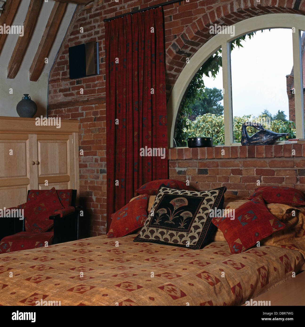 Rideau rouge et fenêtre en demi-lune au-dessus de lit avec couette et  coussins à motifs en chambre grange aménagée Photo Stock - Alamy