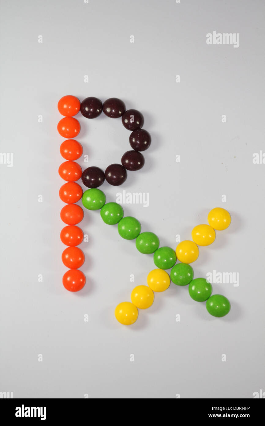Bonbons multicolores disposés en forme de symbole Rx sur fond blanc Banque D'Images
