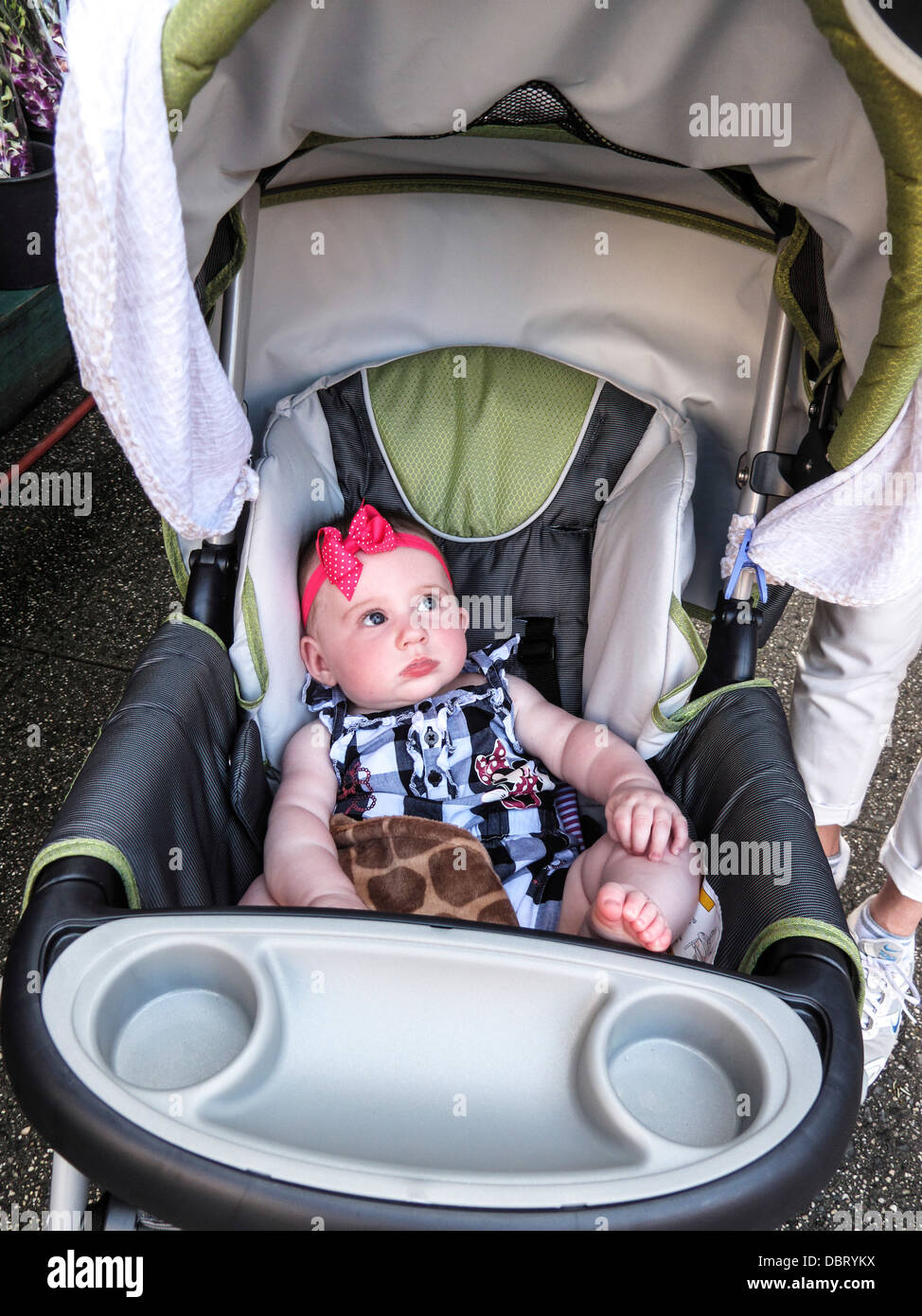 Adorable baby girl animé se trouve dans l'élégant quartier de poussette portant des cheveux rouge à pois bleu barboteuse band & vérifié sur une rue de New York Banque D'Images