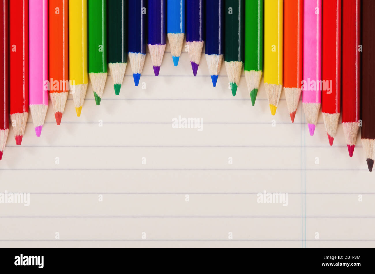 Crayons de couleur dans une rangée contre la lumière jaune des feuilles de carnet Banque D'Images