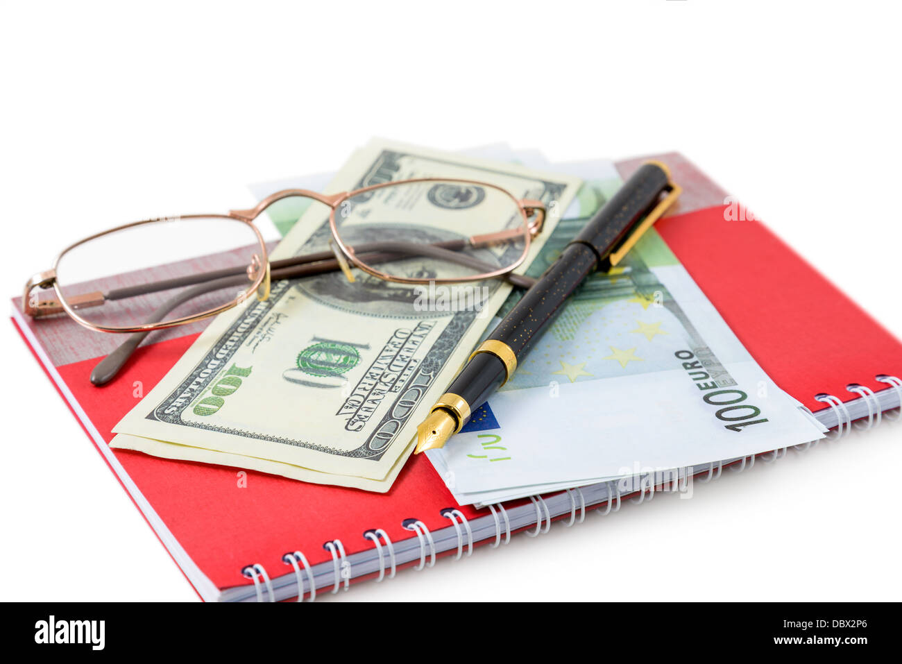 Le stylo, lunettes, dollars, euros sont couché sur un cahier rouge Banque D'Images