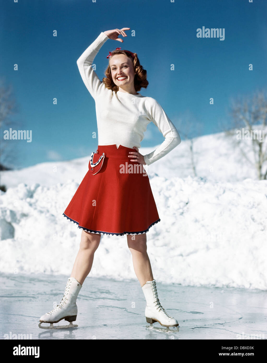 1950 SMILING WOMAN WEARING WHITE SWEATER jupe rouge le patin à glace SUR LA TÊTE DU BRAS posant avec Banque D'Images