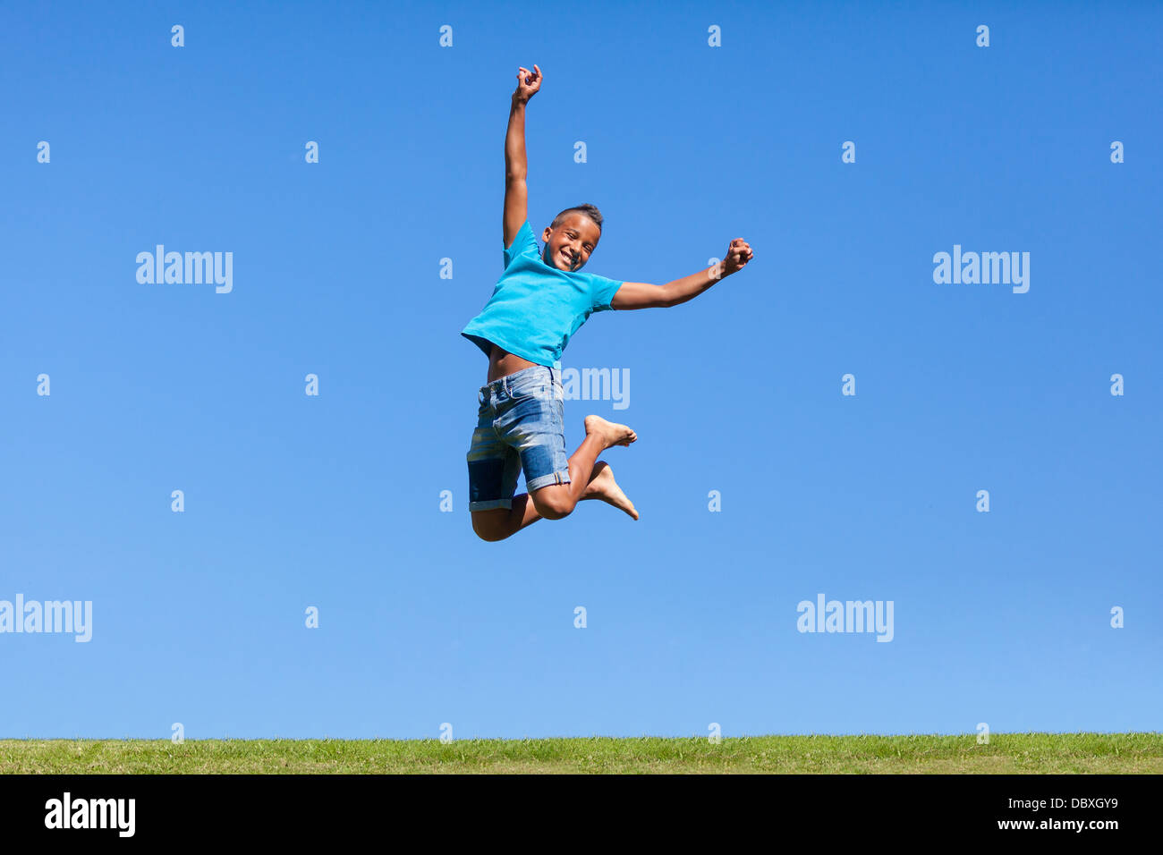 Outdoor portrait of a cute black teenage boy jumping over a blue sky - peuple africain Banque D'Images