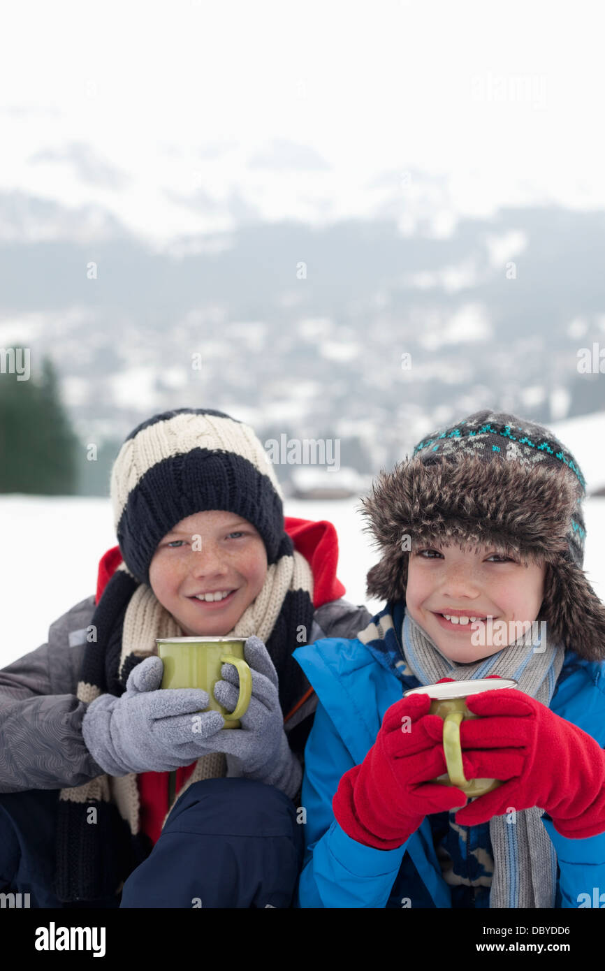 Portrait of smiling boys drinking hot chocolate in snowy field Banque D'Images