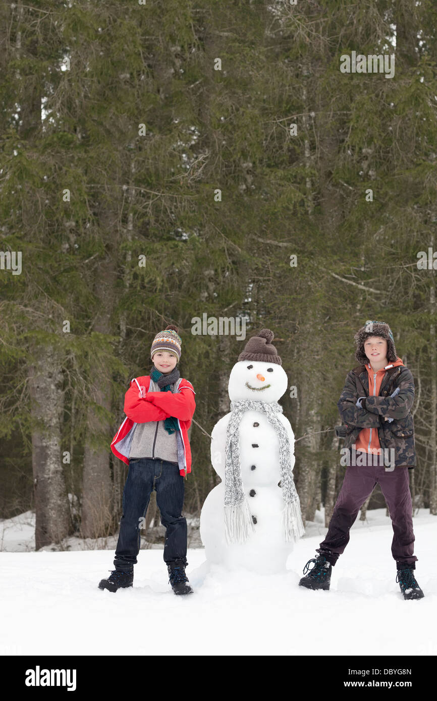 Young Boys à côté de snowman in woods Banque D'Images