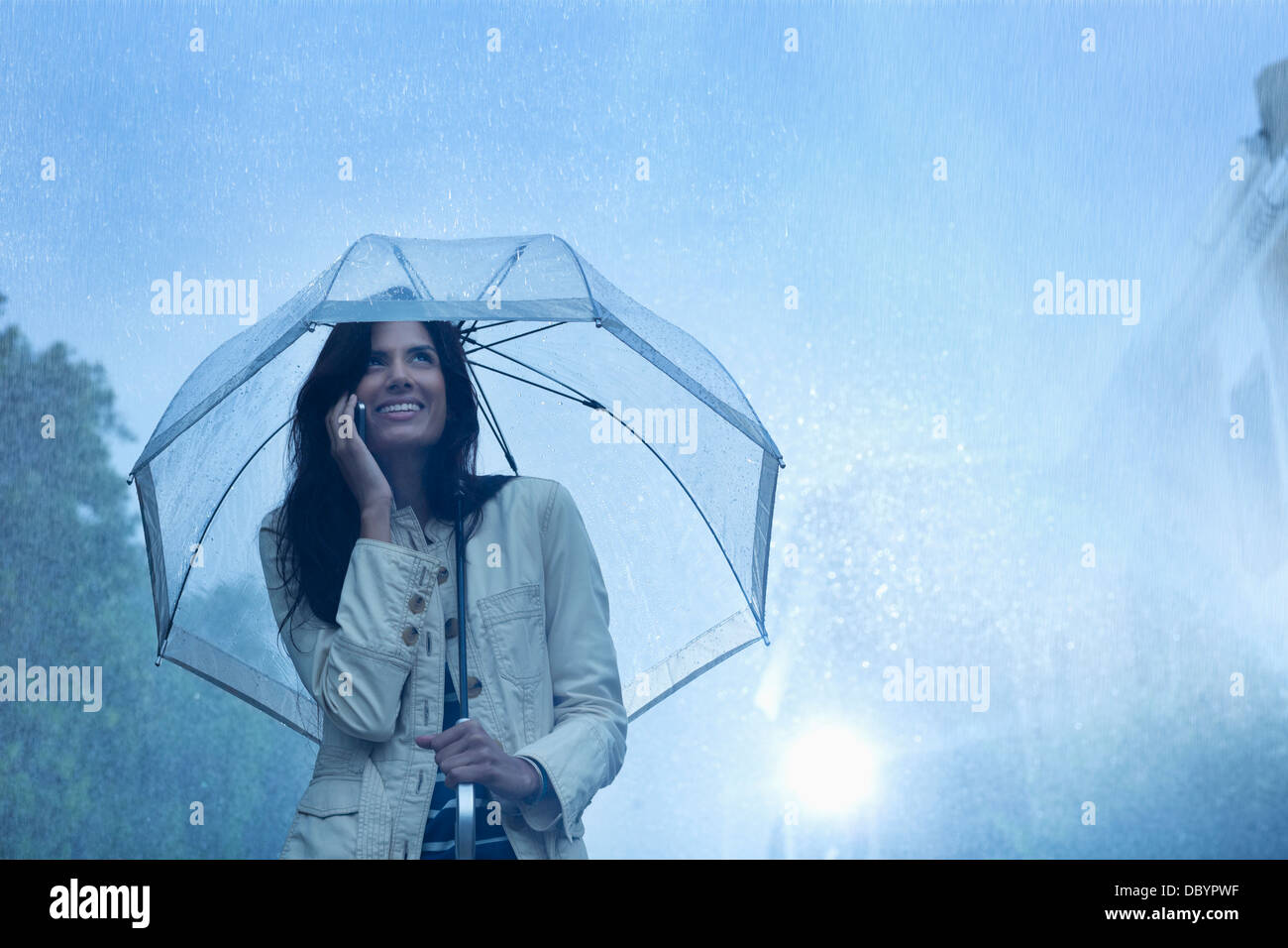 Businesswoman talking on cell phone under umbrella in rain Banque D'Images