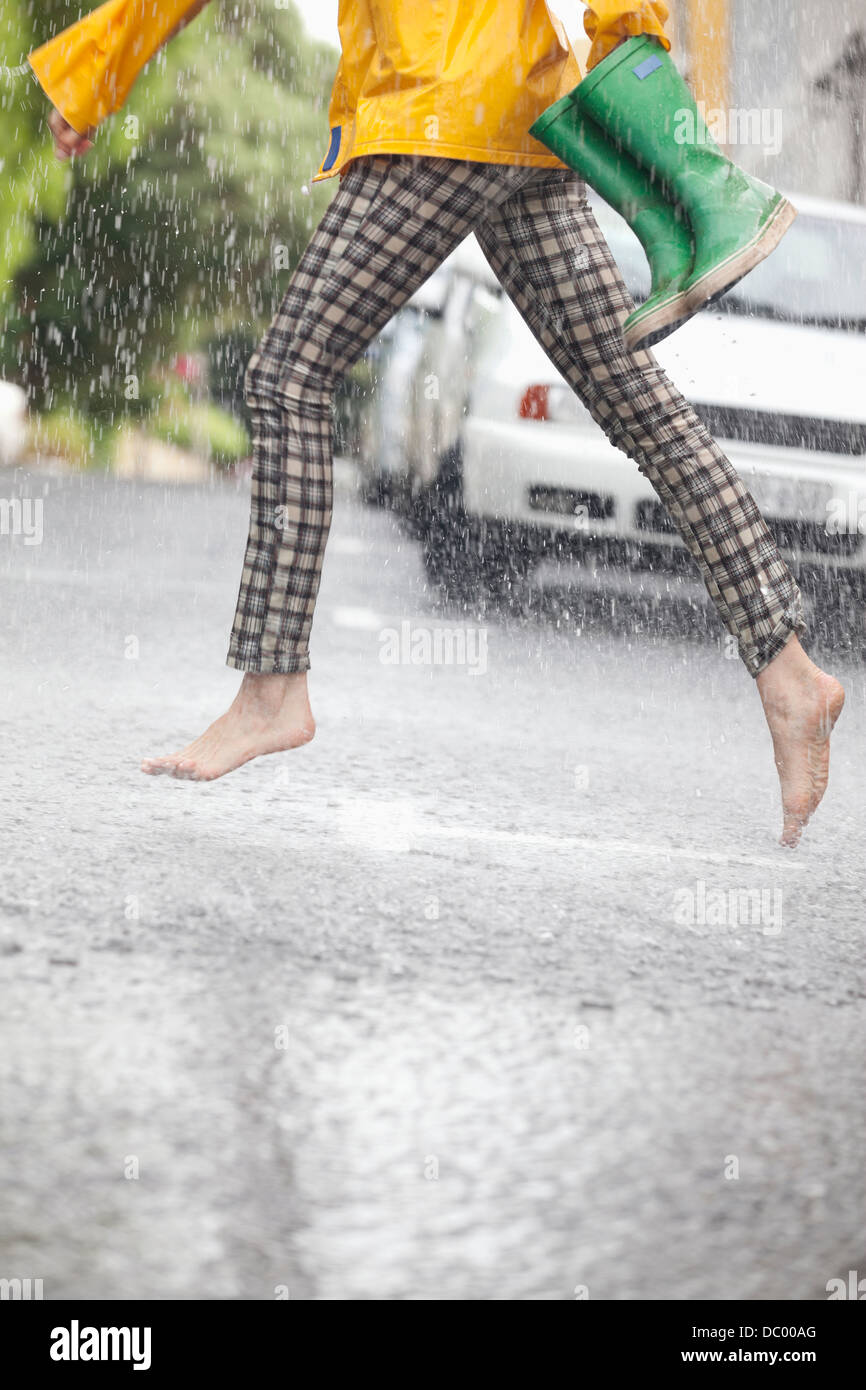 Barefoot running femme de l'autre côté de la rue dans la pluie Banque D'Images
