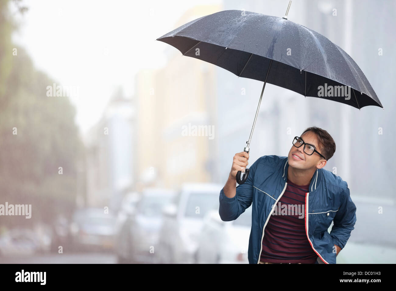Homme avec parapluie à la recherche jusqu'à la pluie en street Photo Stock  - Alamy