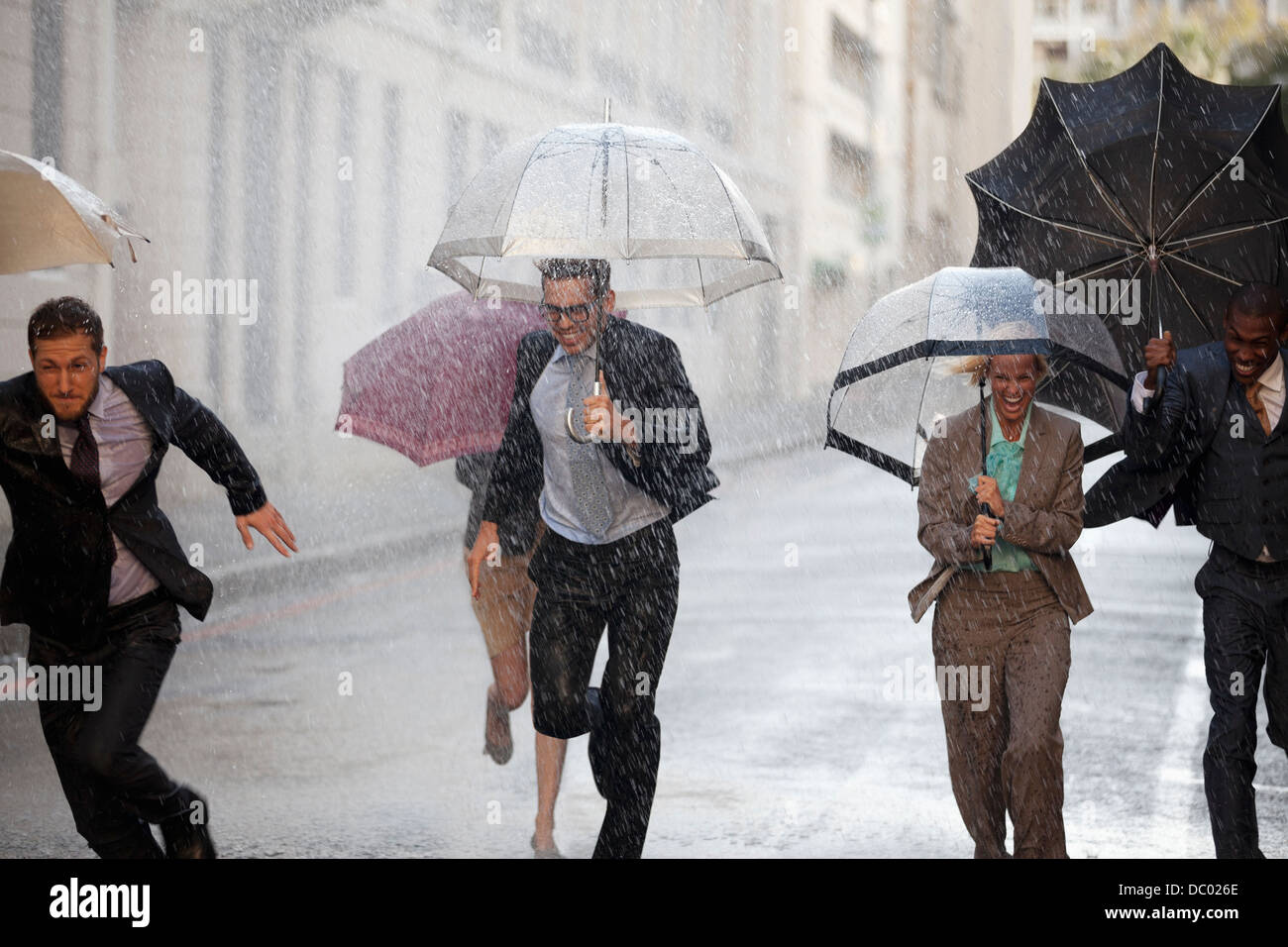 Les gens d'affaires enthousiastes avec parasols fonctionnant à Rainy Street Banque D'Images