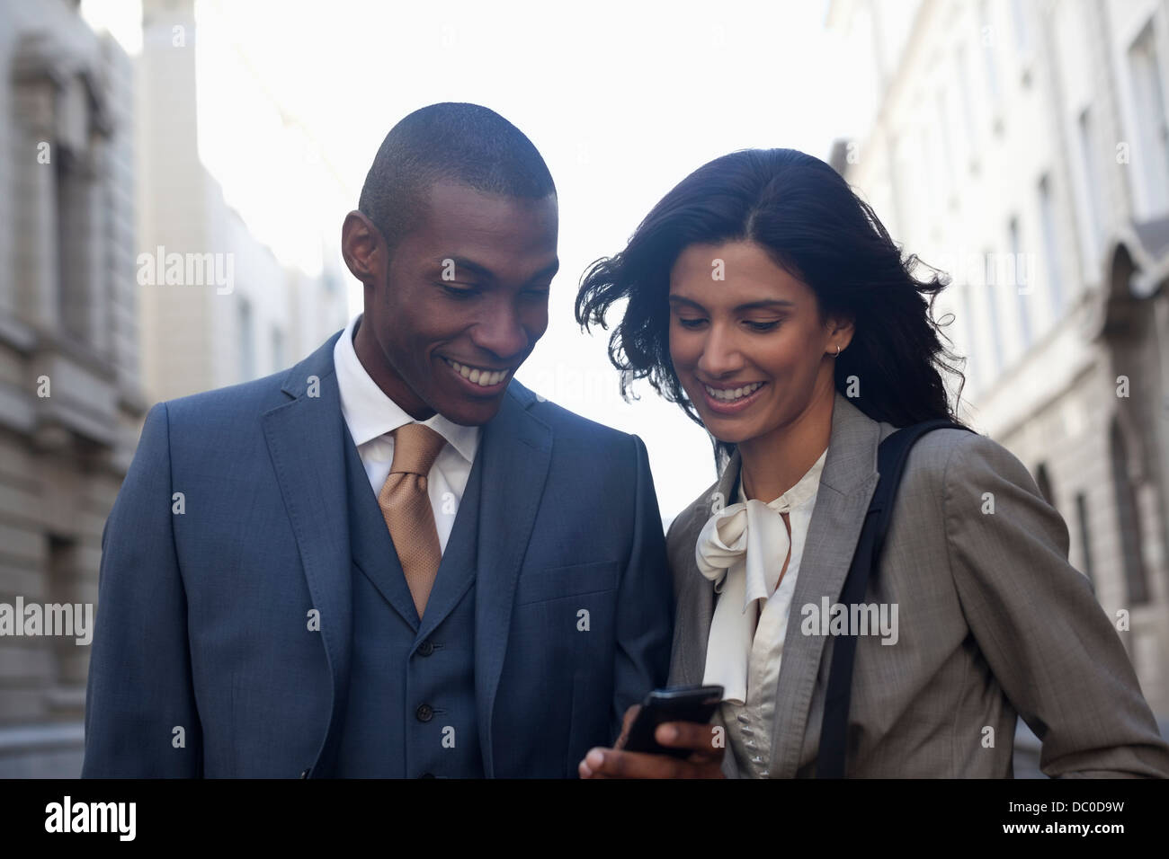 Smiling business people text messaging with cell phone Banque D'Images